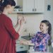 Happy young mother and cute funny daughter playing clapping hands game and have fun while cooking in kitchen at home. Family, cooking and people concept