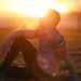 Muscular man sits in rural field at sunset, exhaling visible breath.